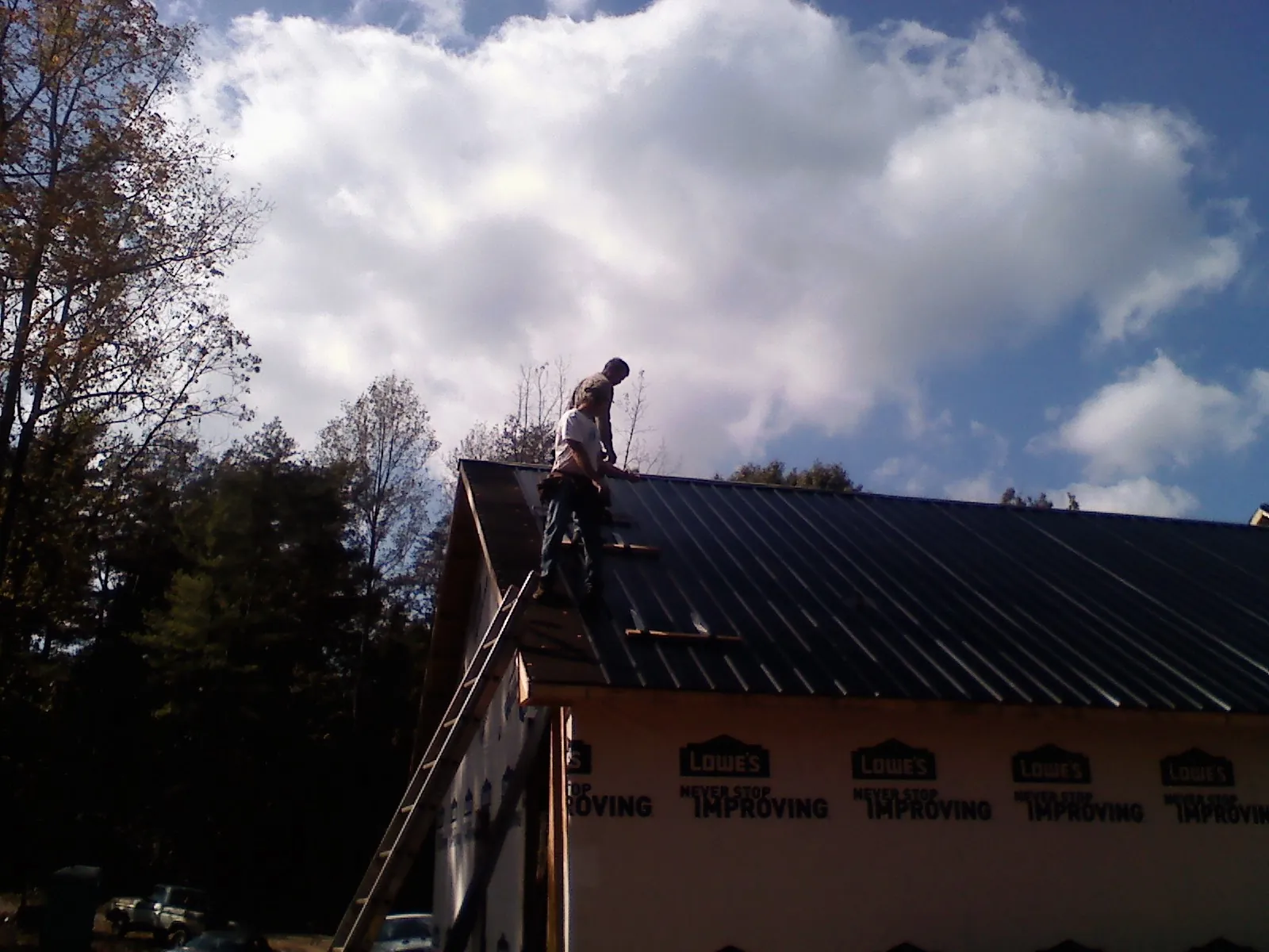 Roofer fastening dark metal panels high against a cloudy sky, from a Roof Inspection job in Chesterfield